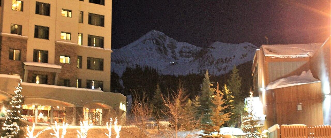 Big Sky Resort's Mountain Village lit for the holidays at night, with Lone Peak behind