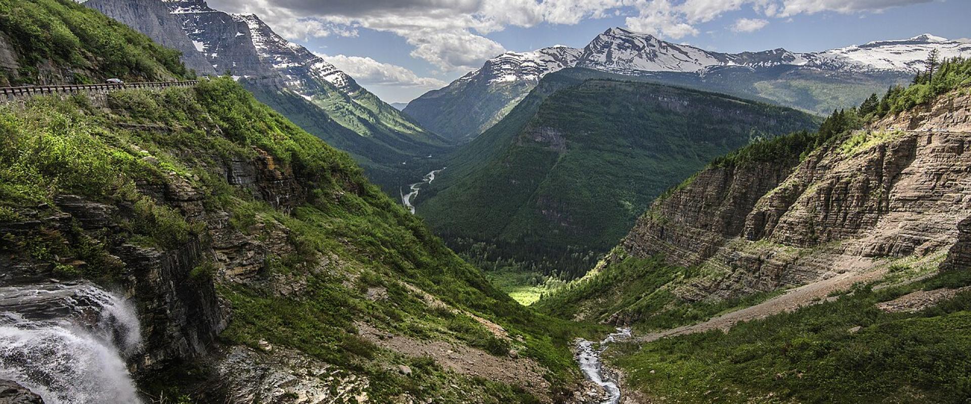 Going-to-the-Sun Road climbing past a waterfall into a green glacial valley in Glacier National Park